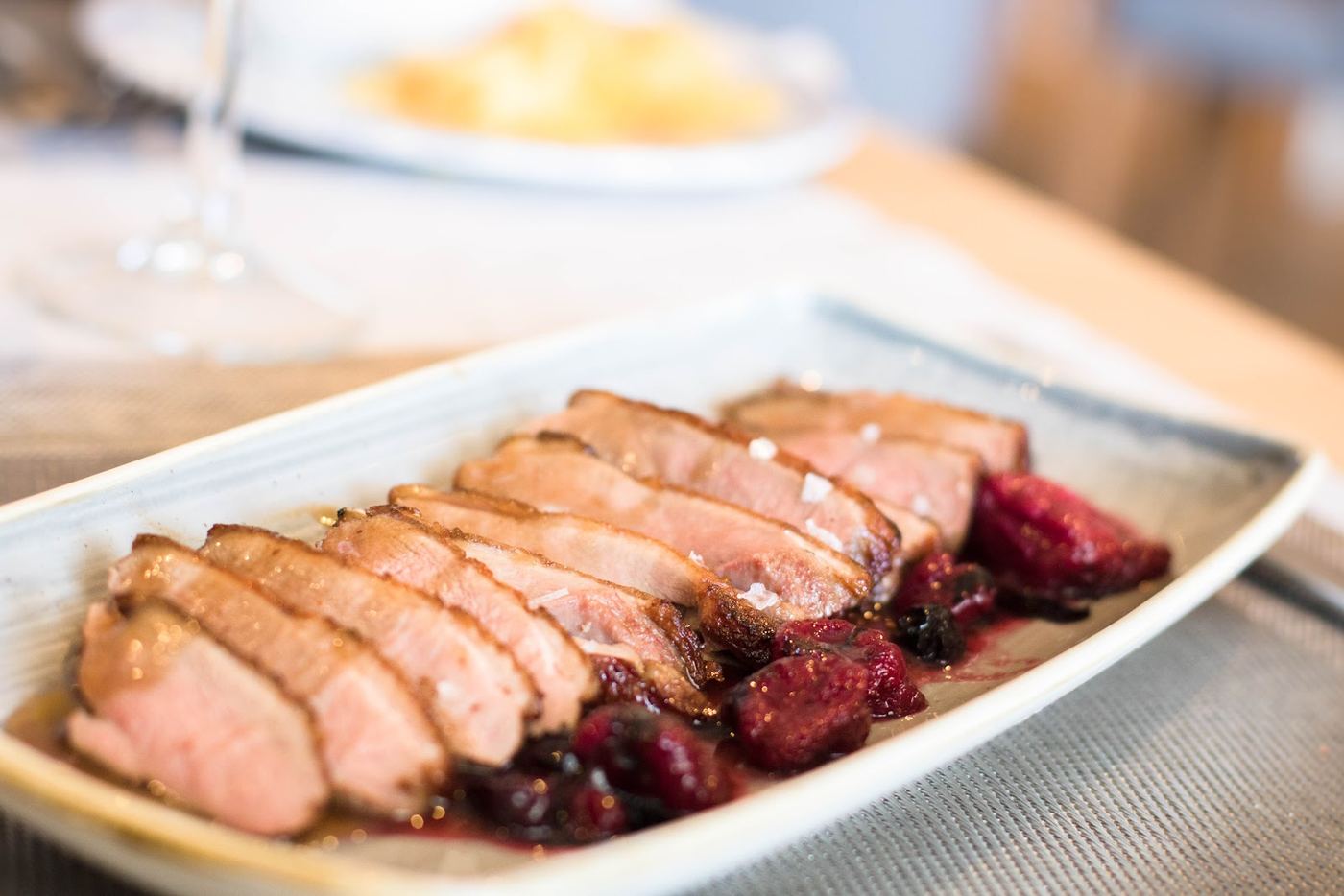 Plato de magret de pato con salsa de frutos rojos, servido con guarnición de verduras