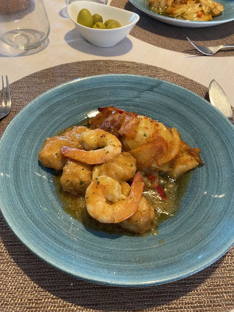 Merluza rebozada con gambas al ajillo, presentada en cazuela de barro